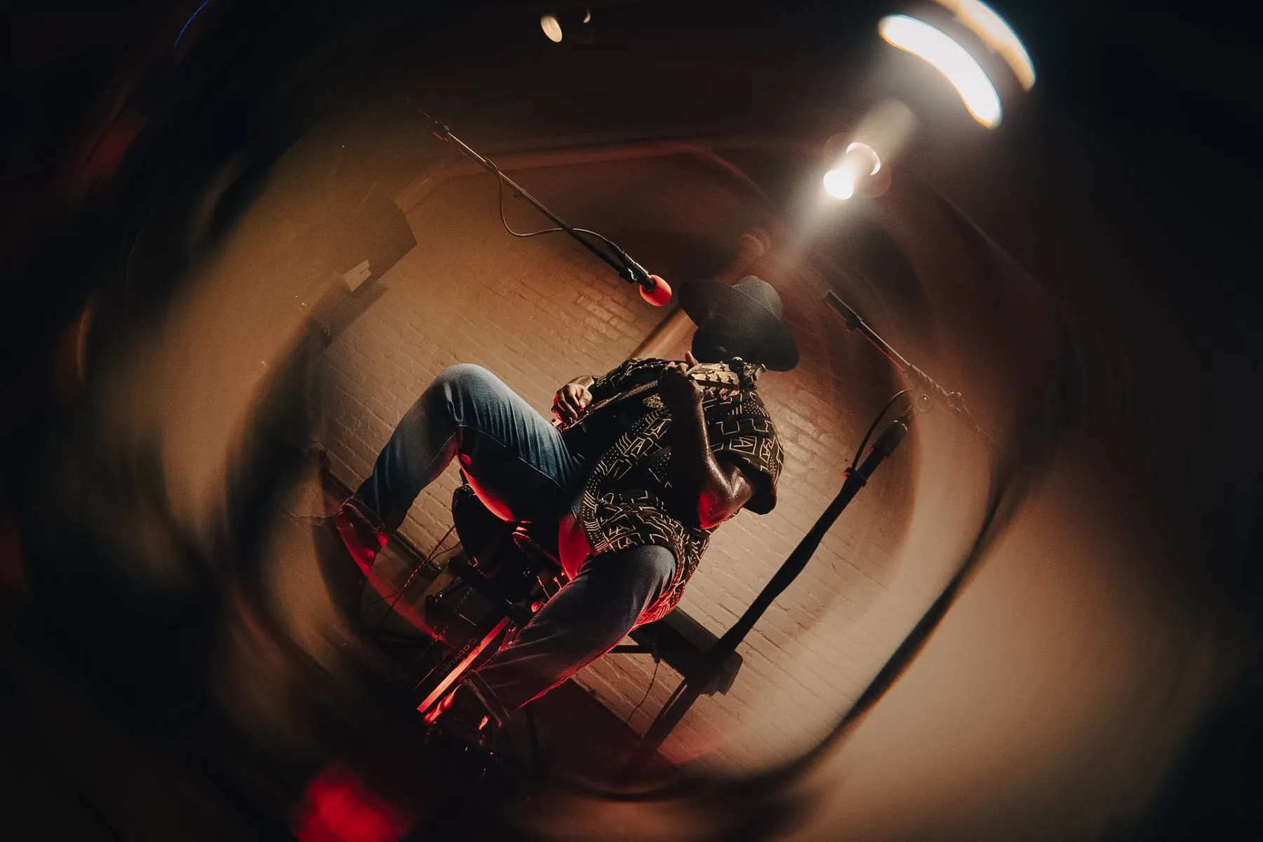 Wide fisheye view of Cuppa T Jones playing guitar under warm red and blue stage light.