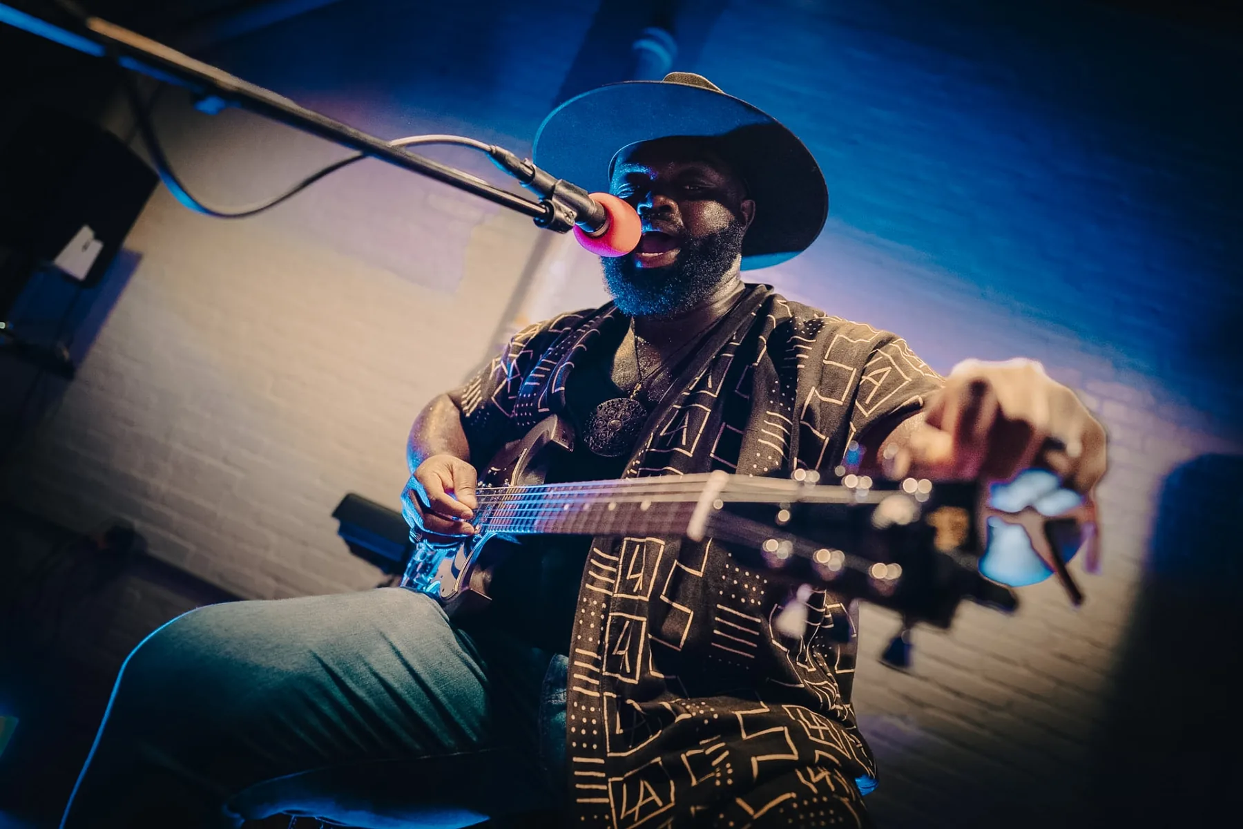 Cuppa T Jones singing into a microphone while playing electric guitar in blue stage light.