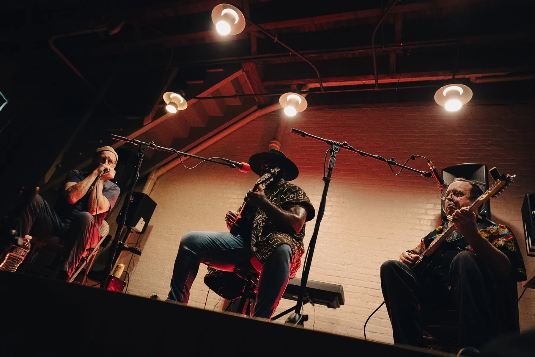 Cuppa T Jones seated center-stage with harmonica and guitar players during an intimate set.