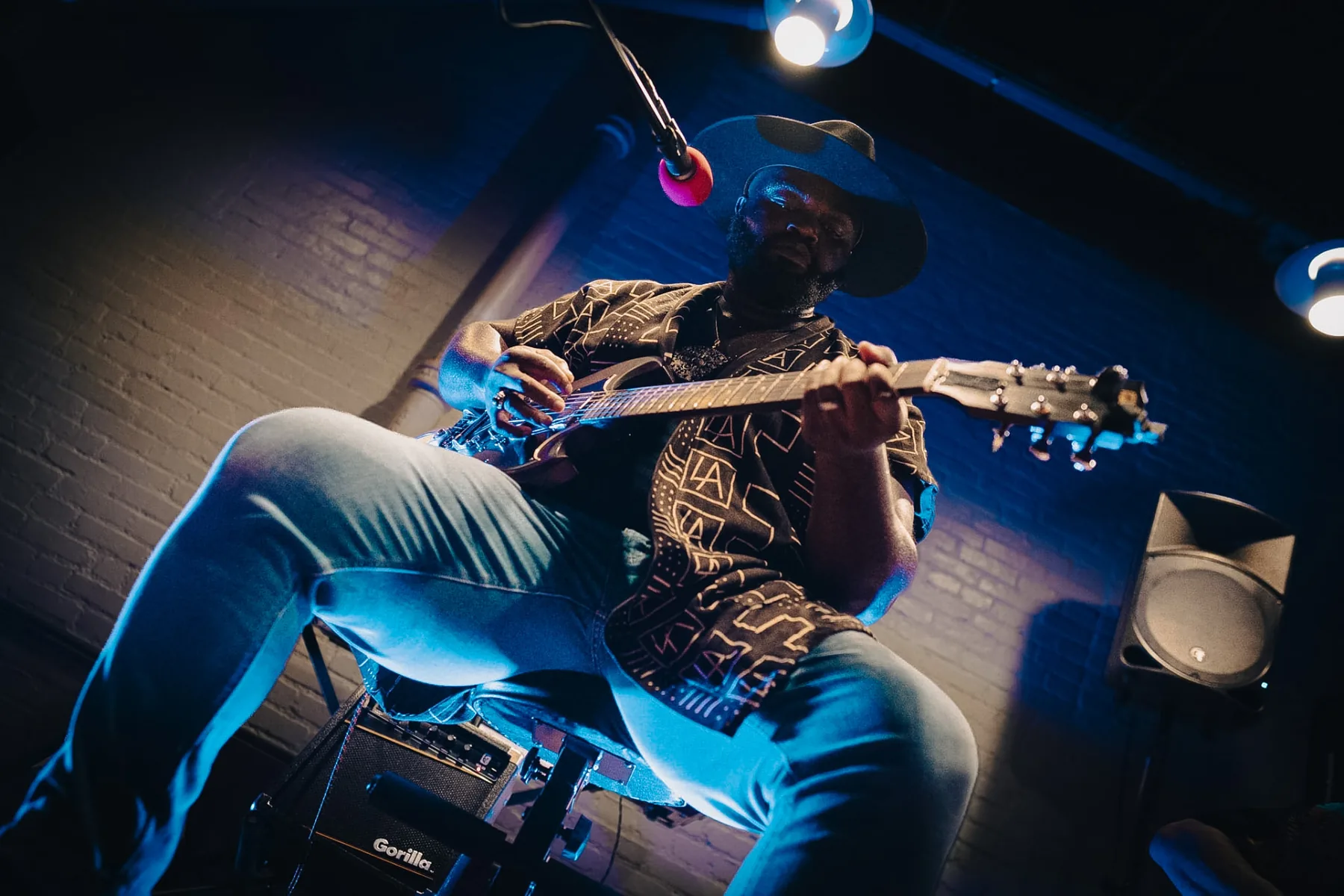 Cuppa T Jones seated, playing electric guitar in blue stage light.