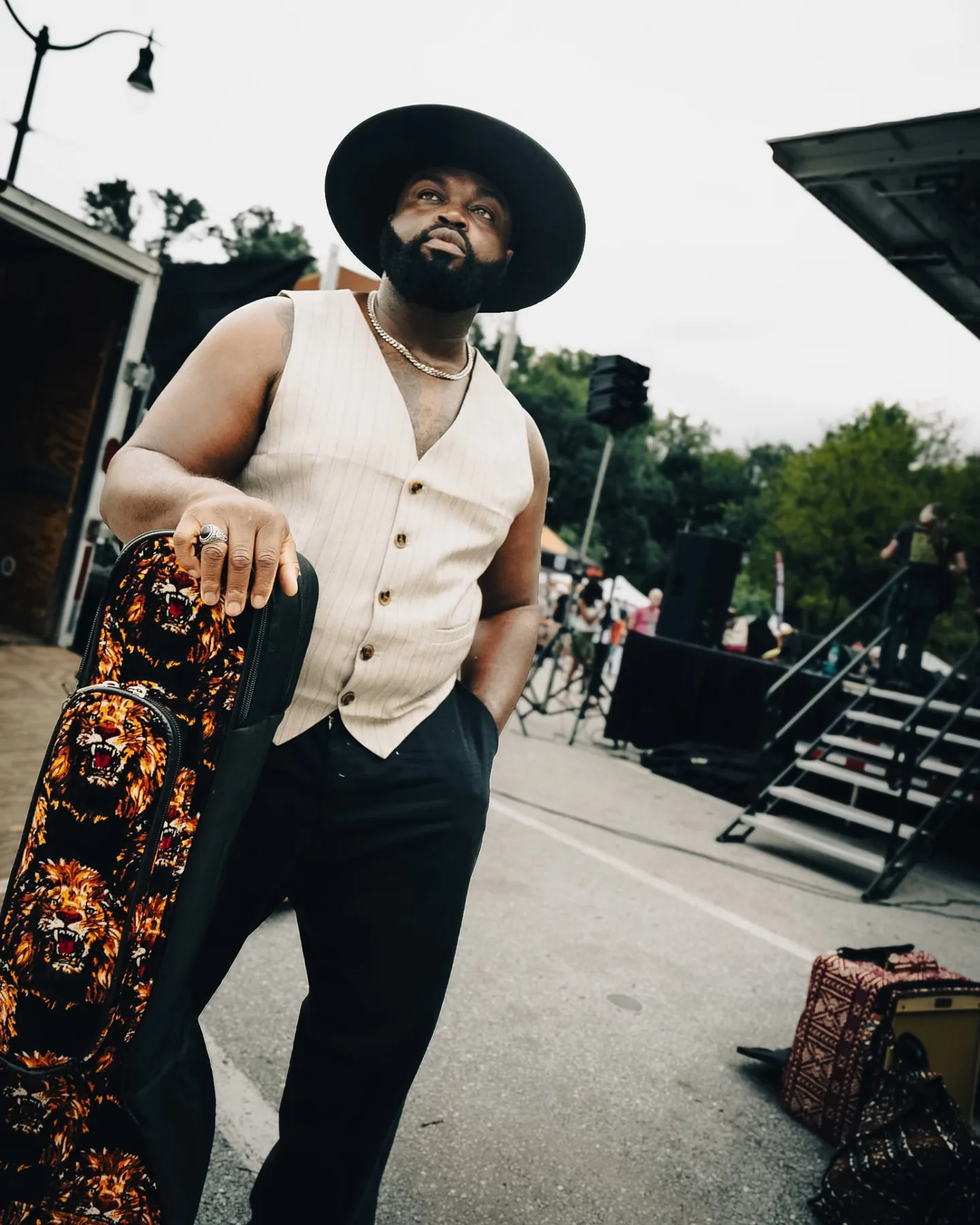 Low-angle portrait of Cuppa T Jones in a wide-brim hat, holding his guitar case before a festival set.