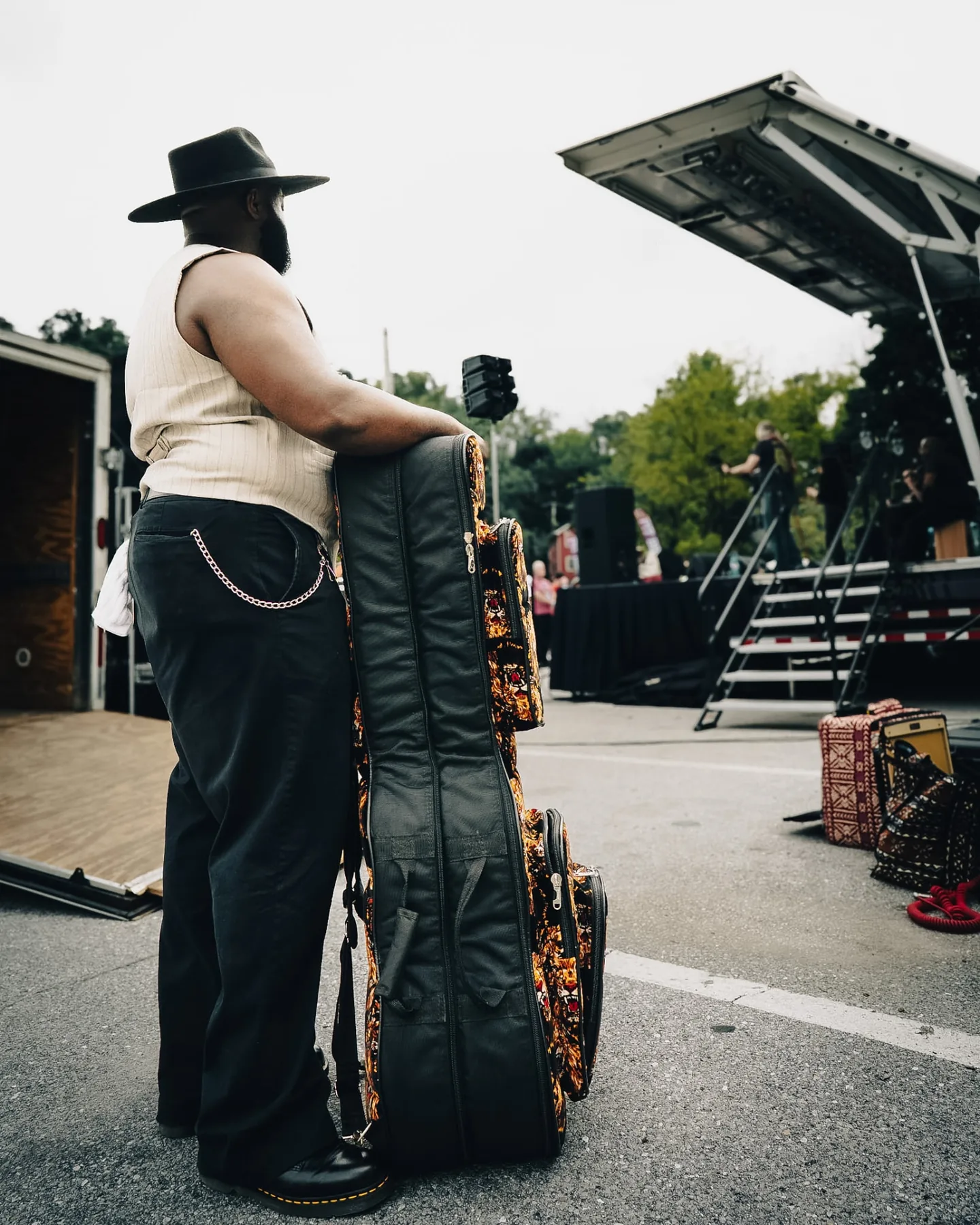 Cuppa T Jones leaning on his guitar case backstage before an outdoor festival set.
